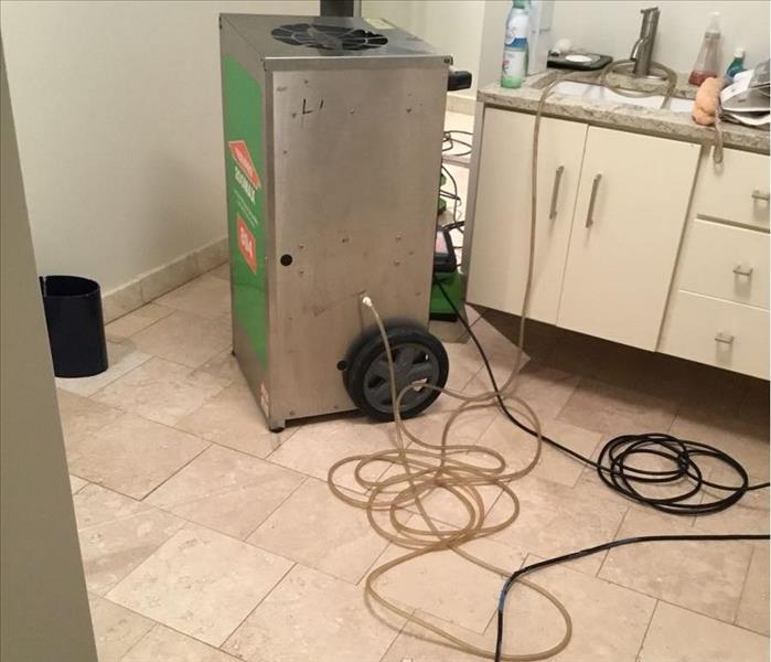 Clean light tan tile with a SERVPRO dehumidifier and an air mover in a bathroom with white cabinets.